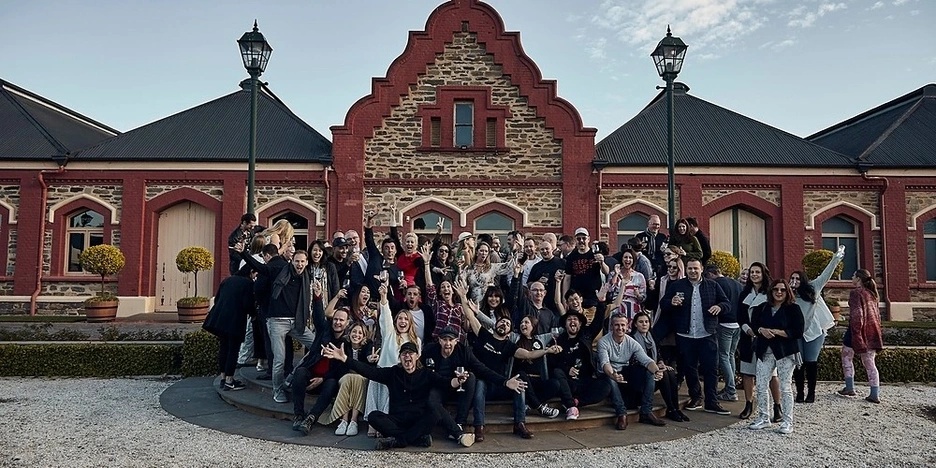 A large group of people standing outside a historic building celebrating with their hands in the air