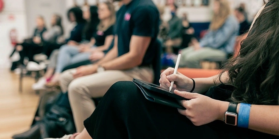Woman sitting in an audience writing on a tablet with stylus