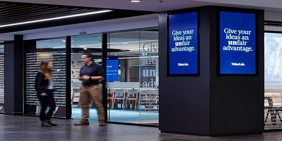 Two people stand outside a glass meeting room next to a tv screen
