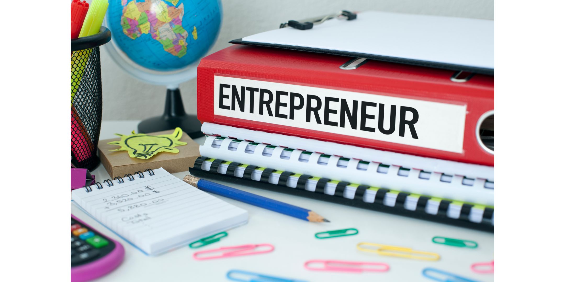 red folder on a desk with the title entrepreneur written on it, surrounded by pens, papers and reminders