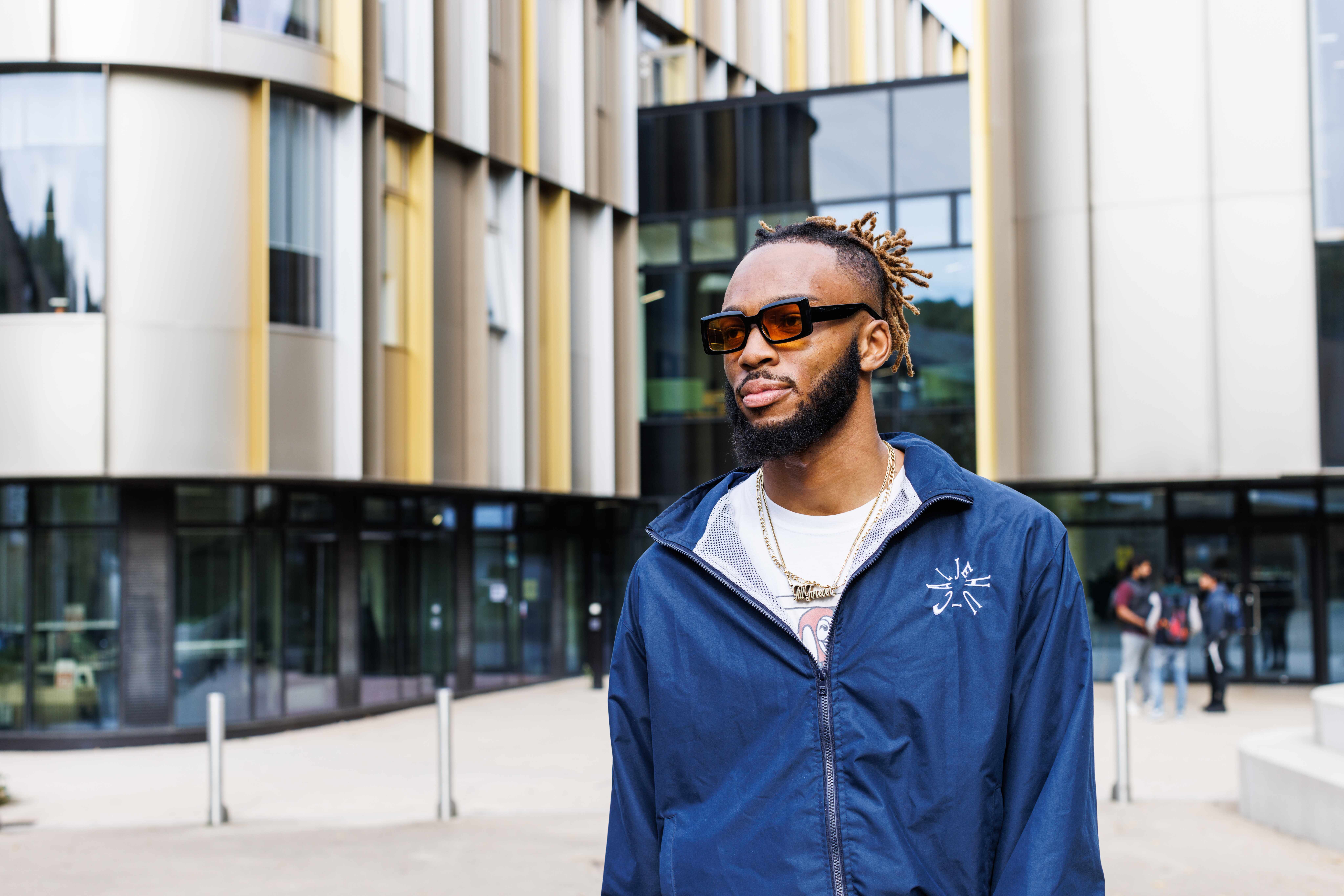 A man in a blue hoodie standing outside the business school building, Sibson, on the University of Kent campus