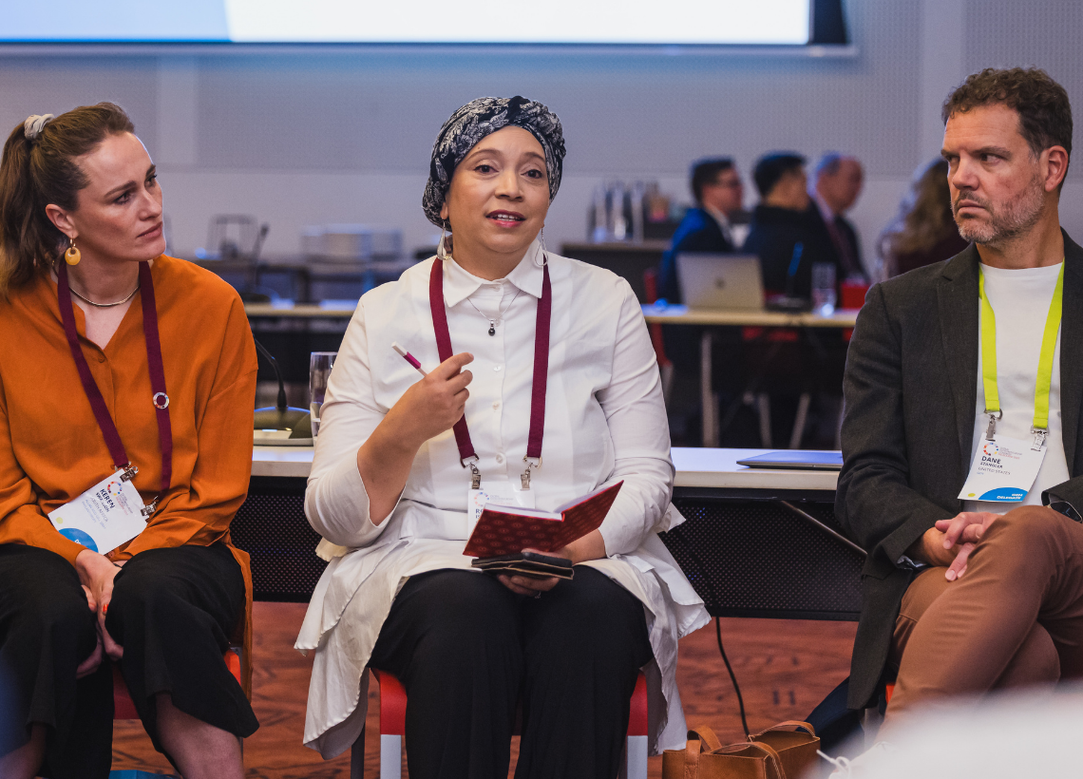 three people sitting in a circle, chatting. one woman holds a book.