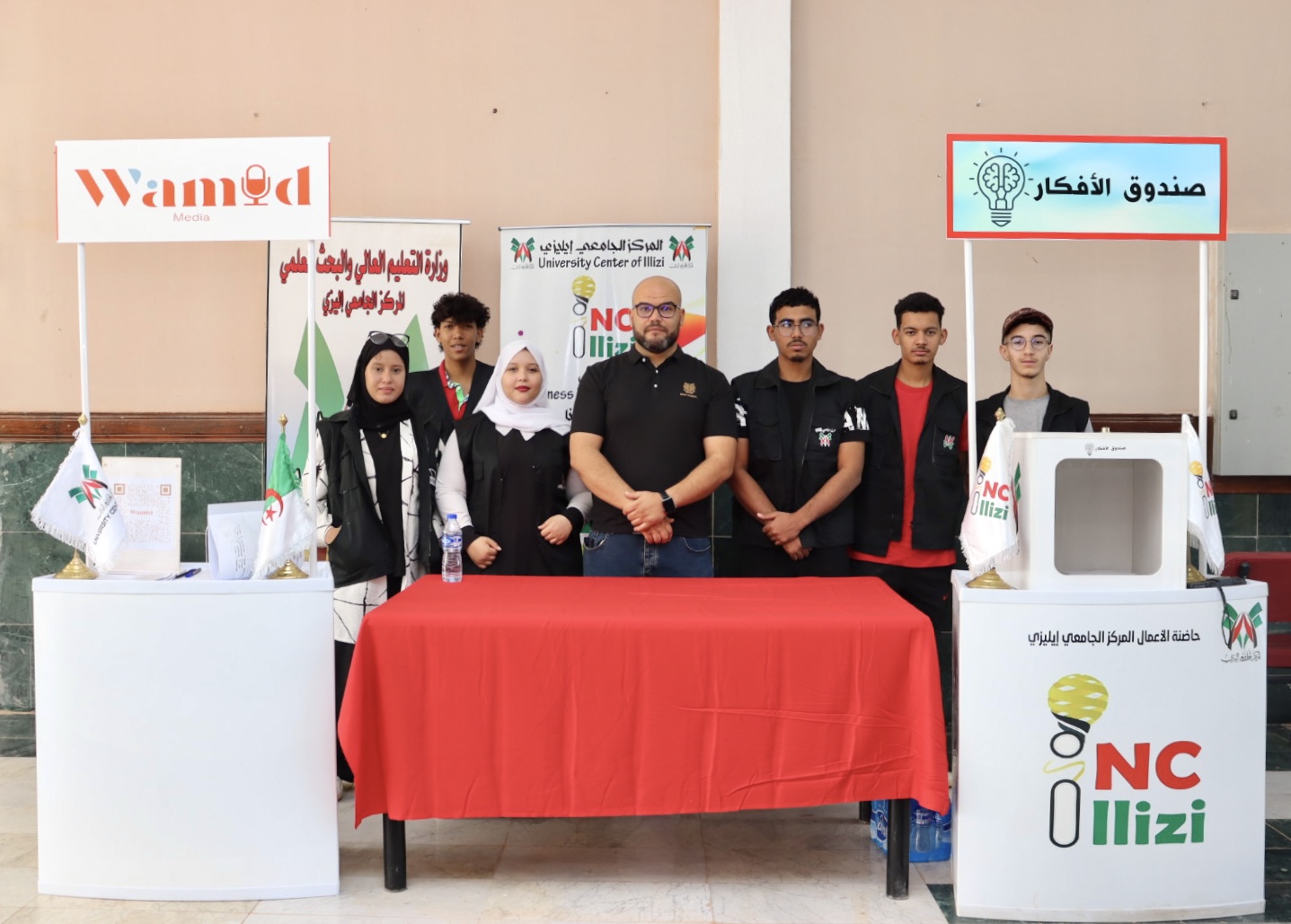 Image of the Business Incubator Director standing with students in front of the Idea Box during Global Entrepreneurship Week at the University Center of Illizi.
