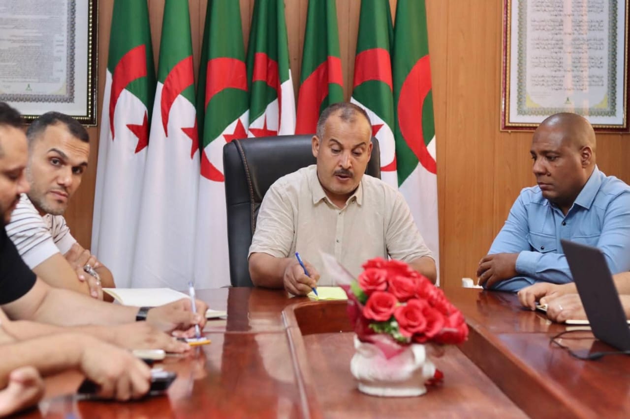 Image of the university interface representatives, institute directors, and deputy directors of the University Center of Illizi attending the coordination meeting to prepare the Global Entrepreneurship Week program, gathered around the table discussing upcoming activities.