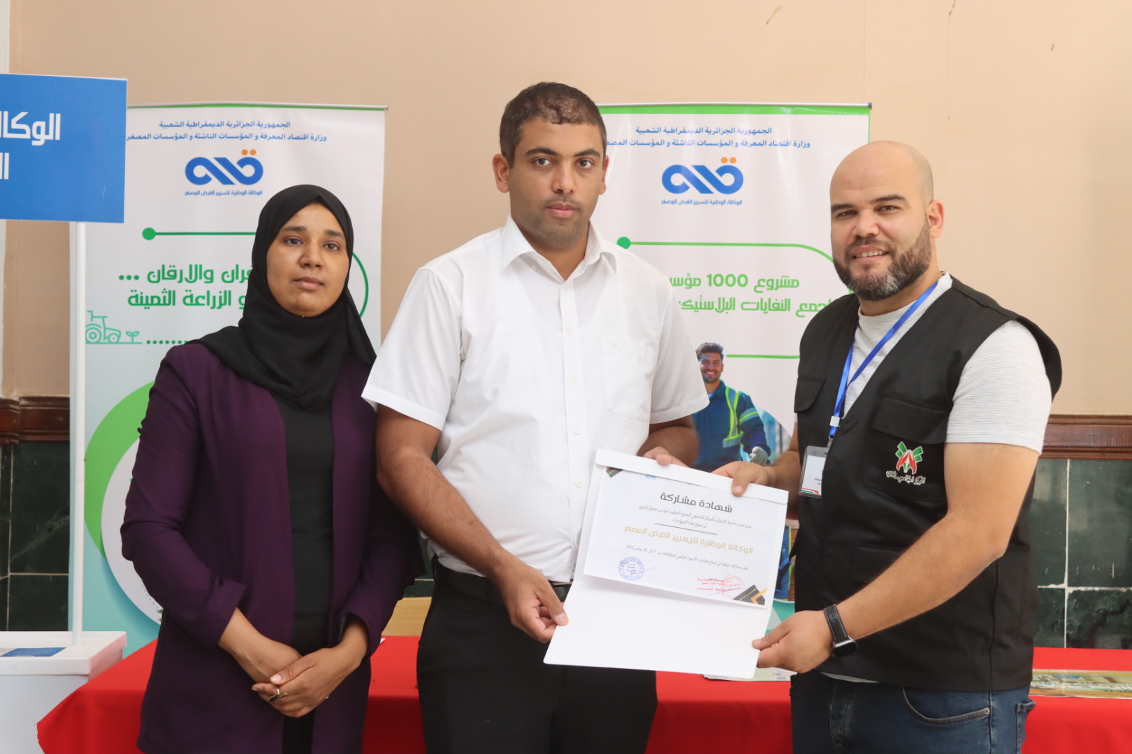 Image showing the Director of the National Agency for Microcredit Management (ANGEM) in Illizi being honored by Dr. Khathir Chine, Director of the Business Incubator, and Dr. Iman Bebba, member of the scientific committee, in recognition of his participation in the professional exhibition during the Global Entrepreneurship Week 2025.
